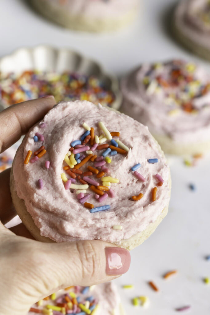 a hand holding a soft frosted sugar cookie.