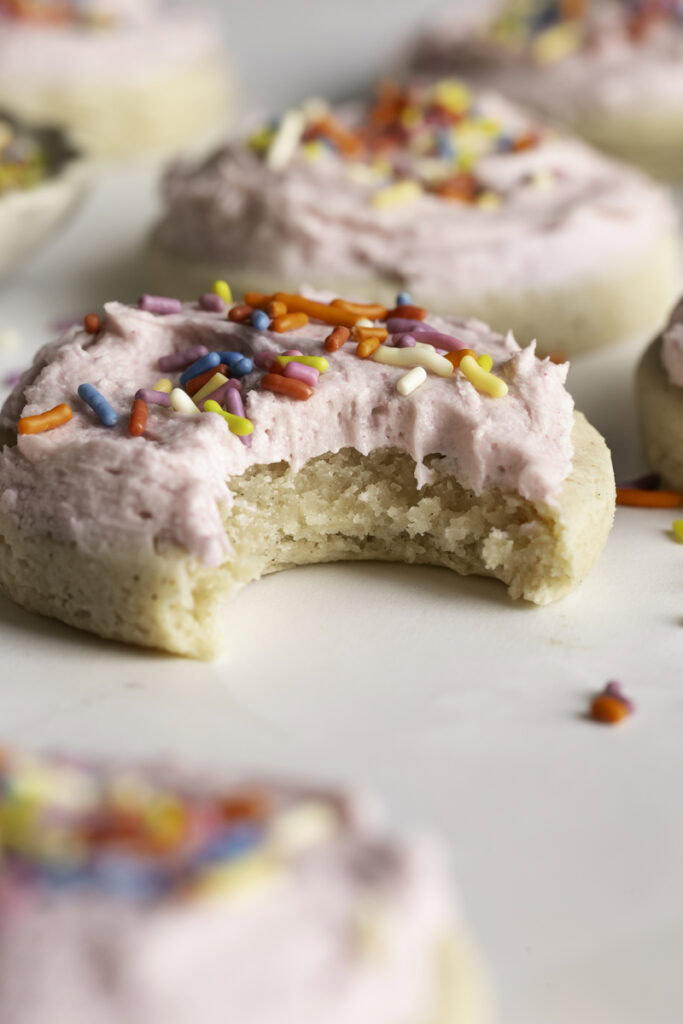 close up of a soft frosted sugar cookie with a bite taken out of it.