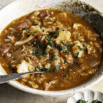 a 3/4 shot of a bowl of vegan cabbage roll soup with a spoon in the bowl and a small dish of chopped parsley.