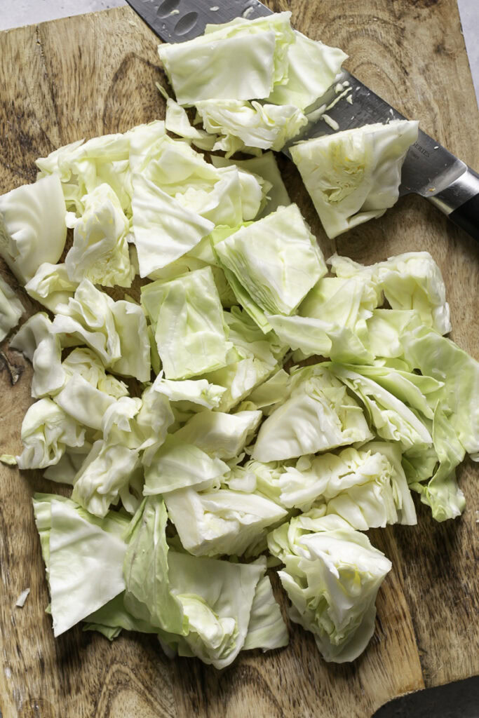 chopped green cabbage on a cutting board with a knife.