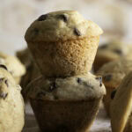A close up of two mini buckwheat flour chocolate chip banana muffins stacked on top of one another.