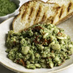 3/4 shot of a close up of spinach pesto butter bean lentil quinoa with two slices of grilled bread.