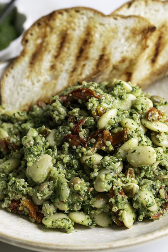 extreme close up shot of spinach pesto butter bean lentil quinoa with two slices of grilled bread.