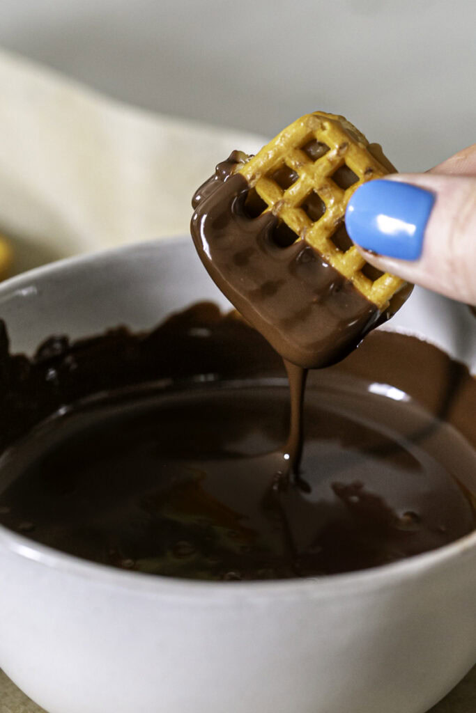 action shot dipping the pretzel bites into melted chocolate.