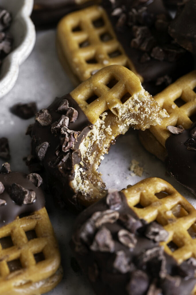 a close up of a Caramel Stuffed Chocolate Dipped Pretzel with a bite taken out of it on top of other pretzel bites.