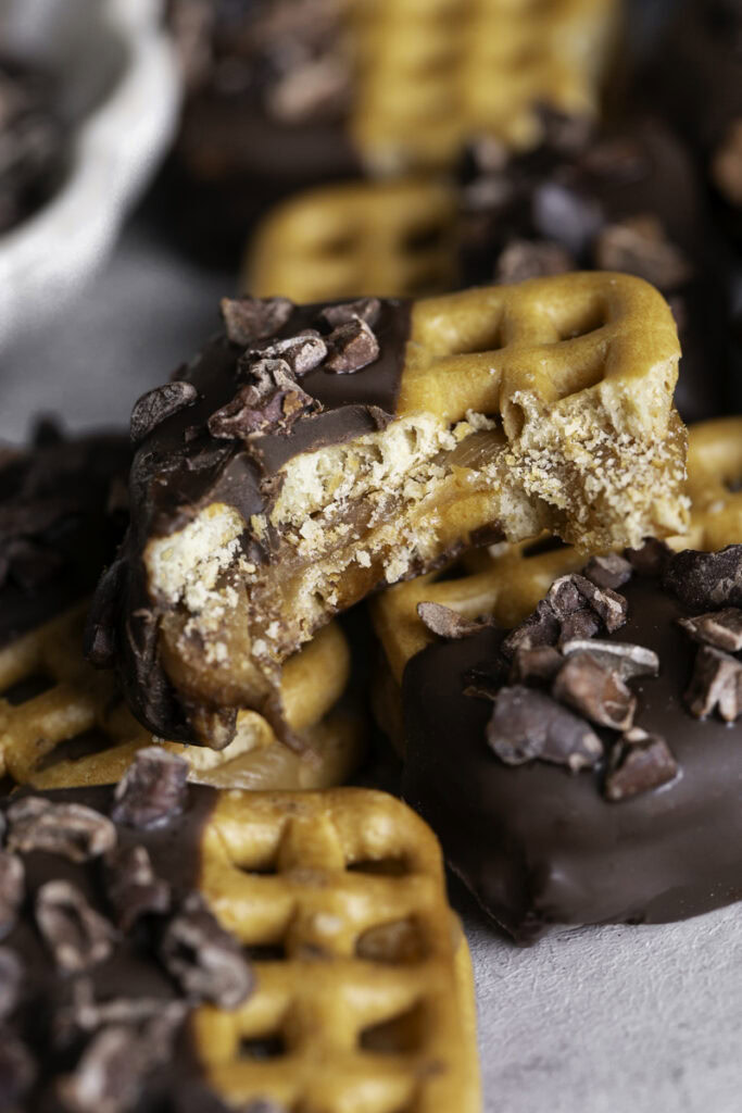 a close up of a Caramel Stuffed Chocolate Dipped Pretzel with a bite taken out of it on top of other pretzel bites.