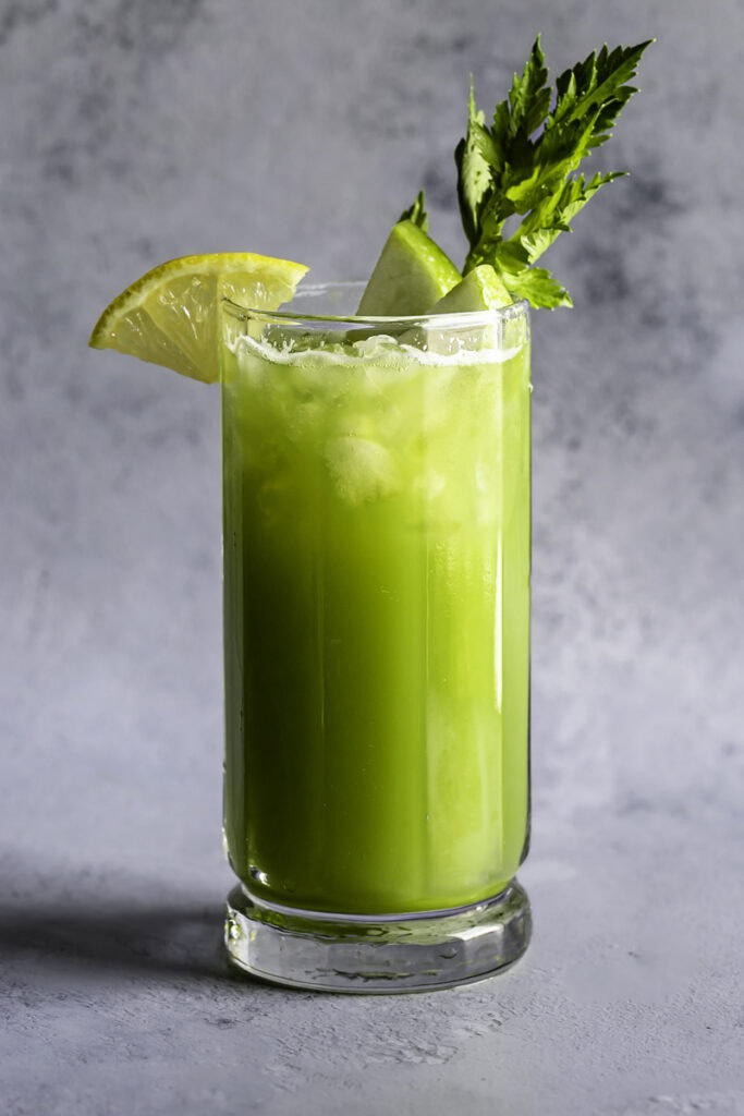 a glass of green apple cucumber lemon celery juice garnished with slices of green apple, lemon, and celery.