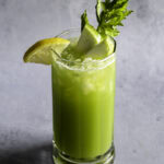 a glass of green apple cucumber lemon celery juice garnished with slices of green apple, lemon, and celery.