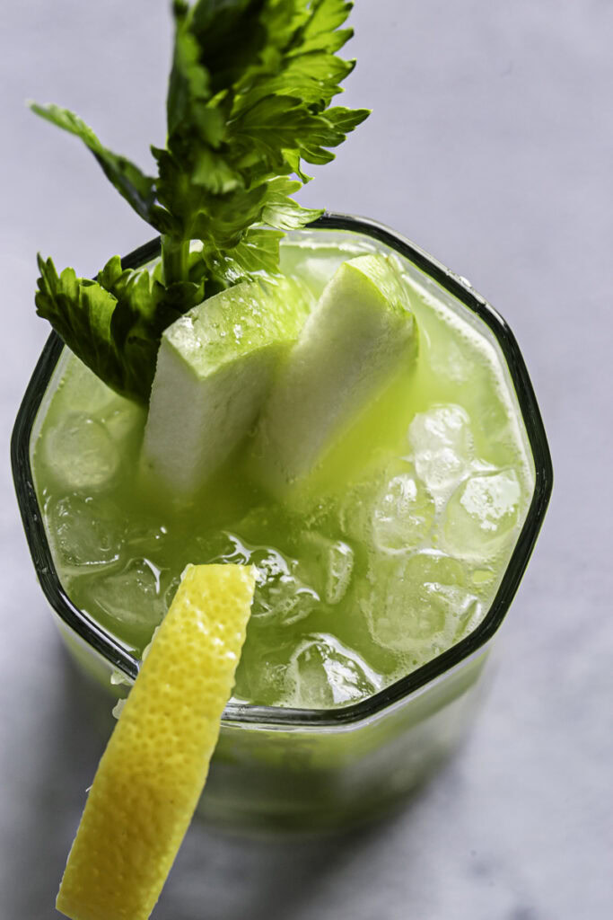 overhead shot of a glass of green apple cucumber lemon celery juice garnished with slices of green apple, lemon, and celery.