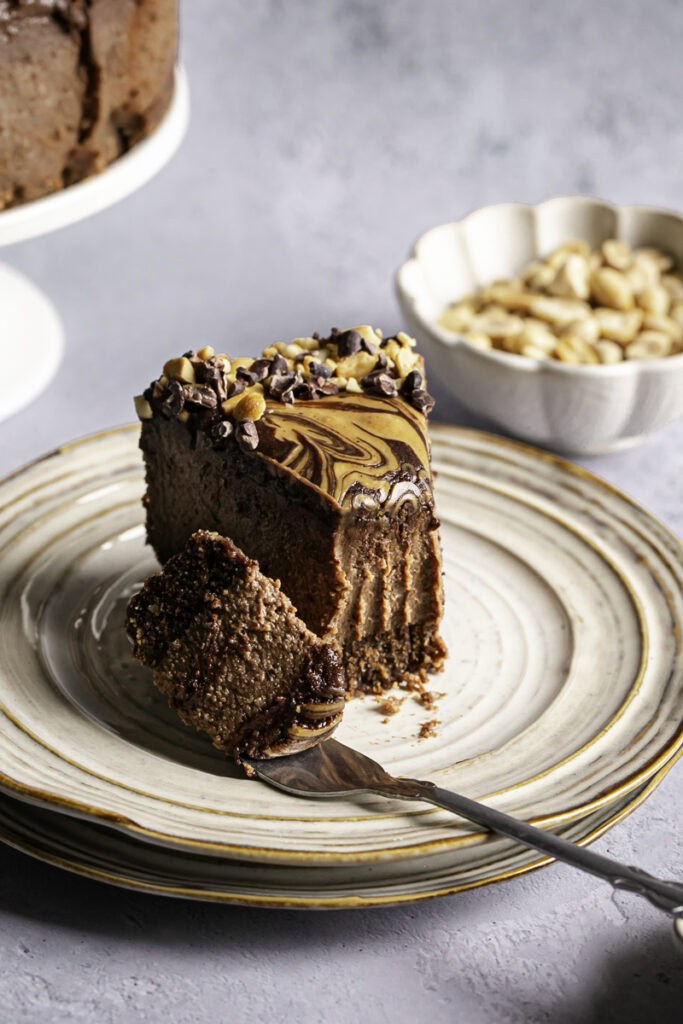 a slice of vegan triple chocolate peanut butter cheesecake on a plate with a piece on a fork.
