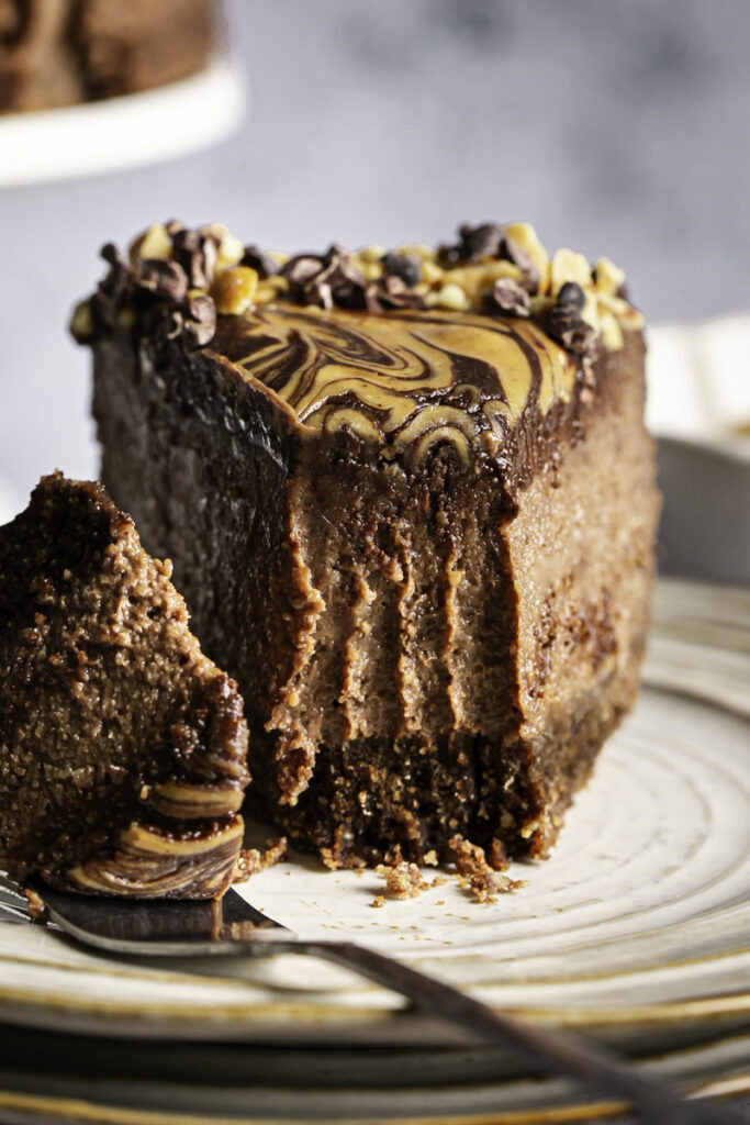a close up of a slice of vegan triple chocolate peanut butter cheesecake on a plate with a piece on a fork.